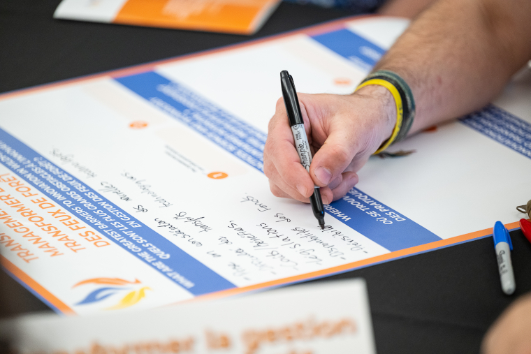 A workshop participant writes notes with a marker on a bilingual poster about barriers to wildfire management innovation.